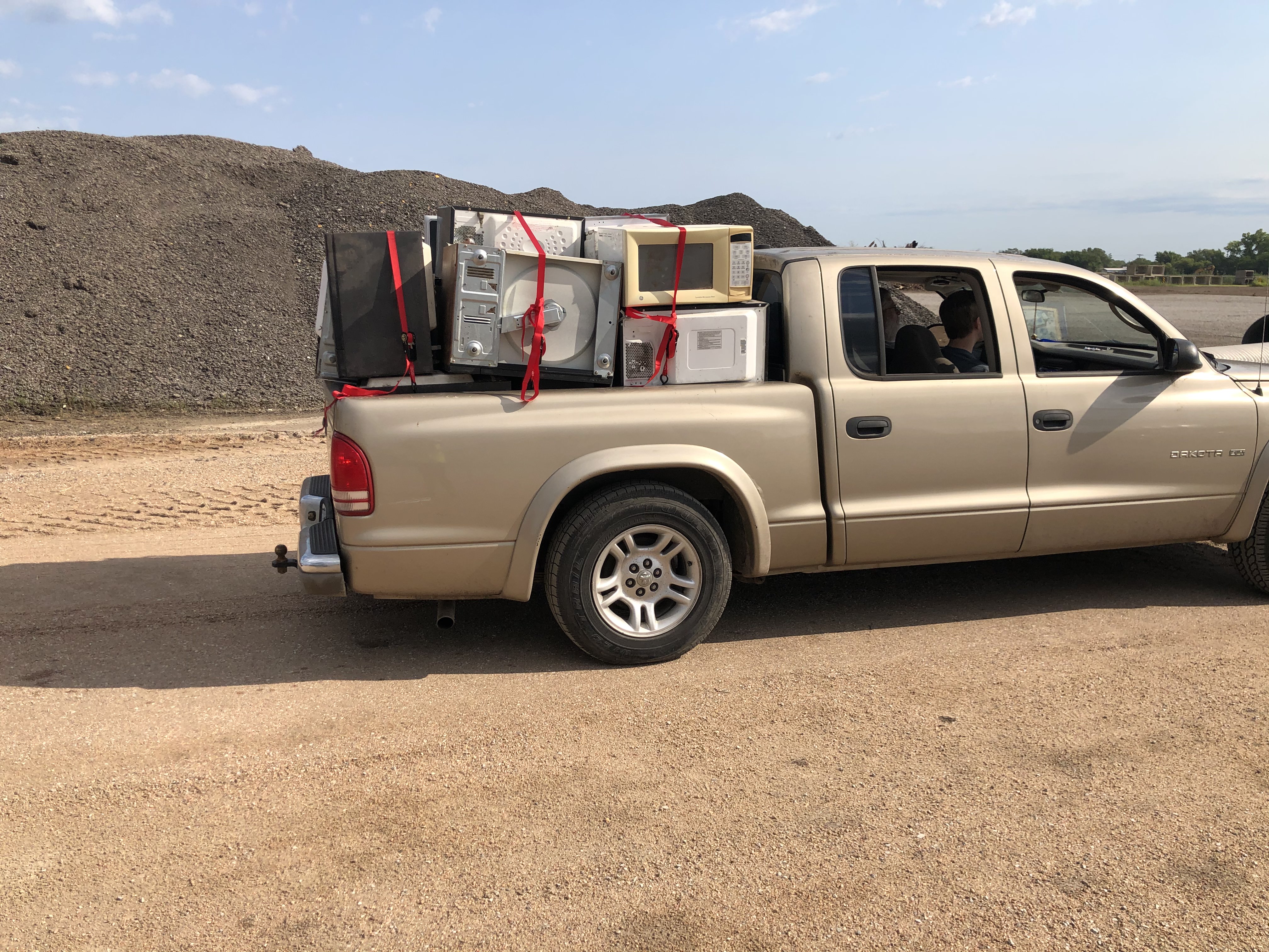 electronic waste, including microwaves, piled high in bed of truck