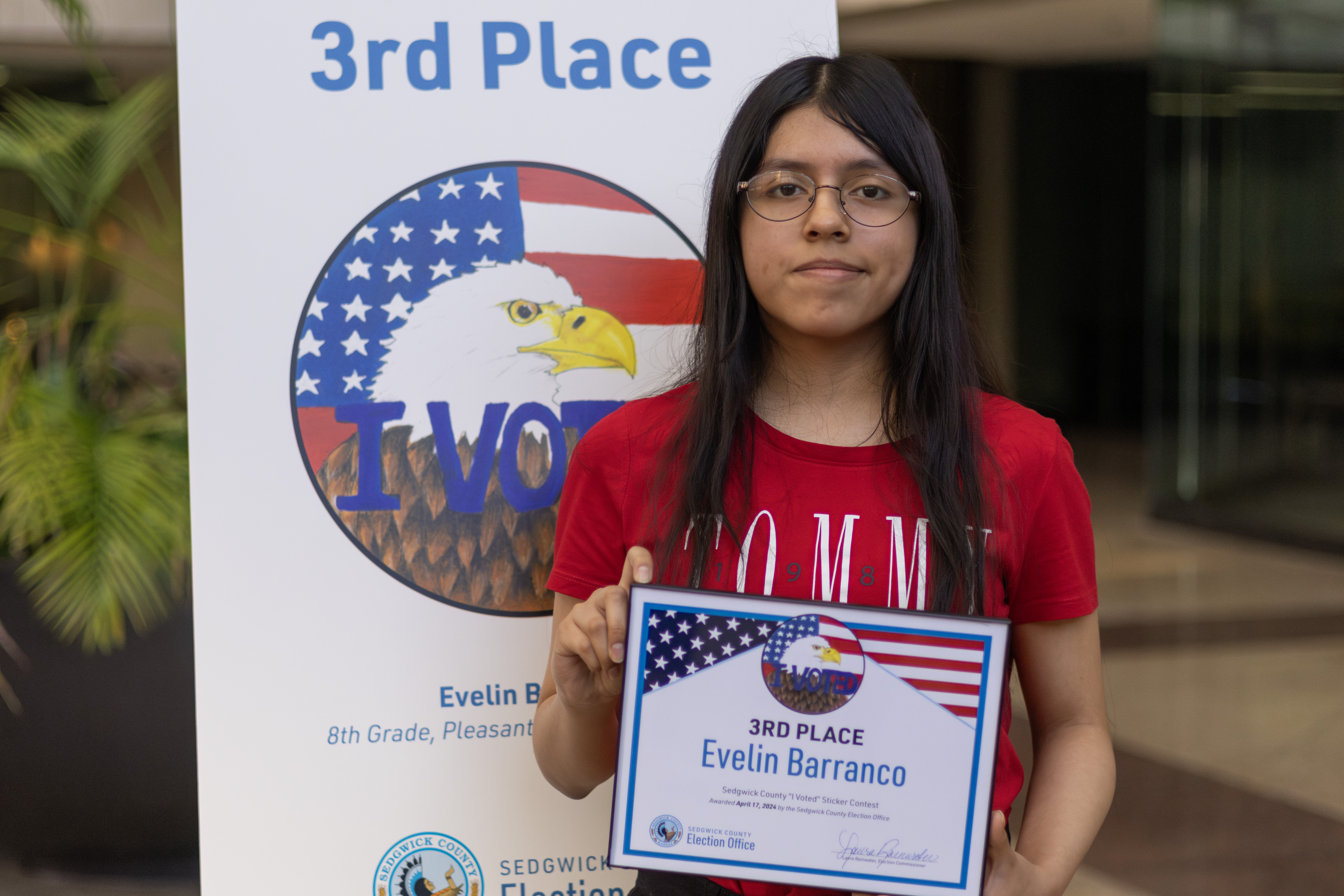3rd place standing in front of her sticker on a tripod. Her sticker is the American flag with a bald eagle and I voted written.